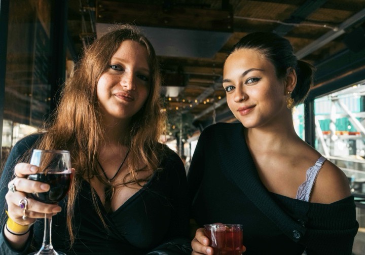 Two friends smiling with a glass of red wine and a soft drink on the Battersea Barge