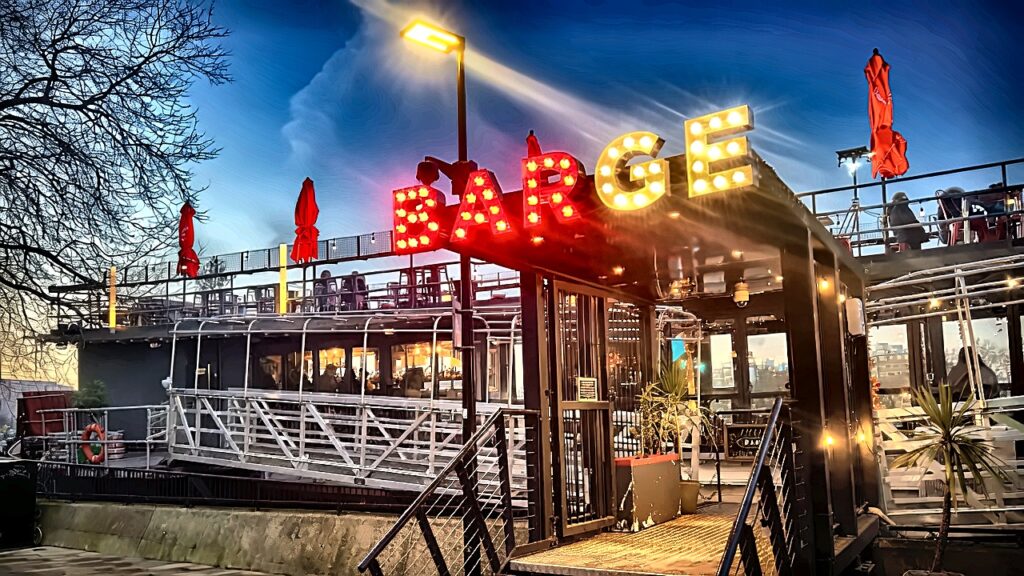 The Comedy Boat lit up on the Thames at Battersea in the evening